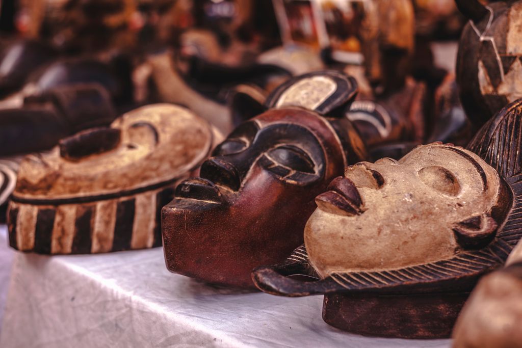 Carved wooden masks with intricate designs displayed at a vibrant market.